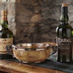 A quaich drinking cup on a table with a bottle of Redbreast 12 and a bottle of Ardbeg Ten whiskies.