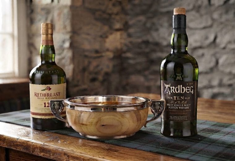 A quaich drinking cup on a table with a bottle of Redbreast 12 and a bottle of Ardbeg Ten whiskies.